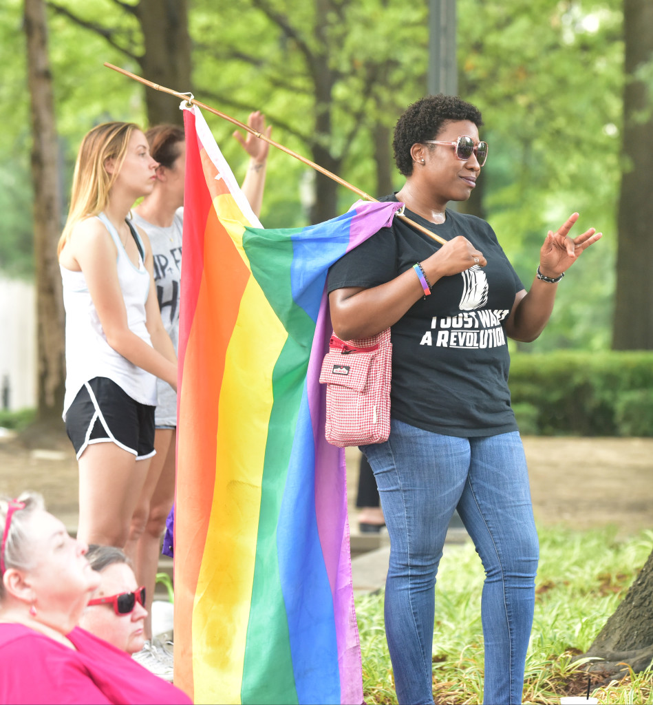 Gina Mallisham draped in a rainbow flag waves to a friend in the crowd. Central Alabama Pride held a remembrance and candle light vigil for those killed and injured in an Orlando, Florida nightclub. The names of the victims were read aloud on the steps of the Jefferson County Courthouse and a rainbow banner was draped over the Birmingham City Hall entrance. (Frank Couch / The Birmingham Times)