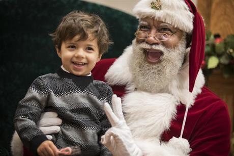 In this Thursday, Dec. 1, 2016 photo, Larry Jefferson, playing the role of Santa, smiles with Jack Kivel, of Prior Lake, for photos at the Santa Experience at Mall of America, in Bloomington, Minn. The nation's largest mall is hosting its first-ever black Santa Claus this this weekend. (Leila Navidi/Star Tribune via AP)