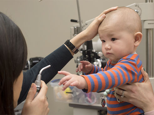 Becky Luu, O.D., checks six month old infant's eye coordination. The infant shows that he can reach for an object, an important six month developmental milestone, and that he has very useful 3-D vision.  (UAB)