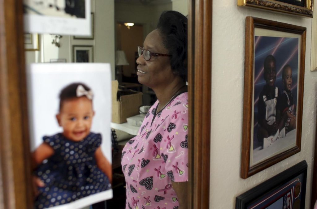 In this photo taken Oct. 18, 2016, Gwen Strowbridge, 71, poses for a photograph among photos of her grandchildren wearing her work uniform at her home in Deerfield Beach, Fla. Strowbridge works six days a week caring for a 100-year-old woman. She has worked all her life and plans to work until she can't physically work anymore. (AP Photo/Lynne Sladky)