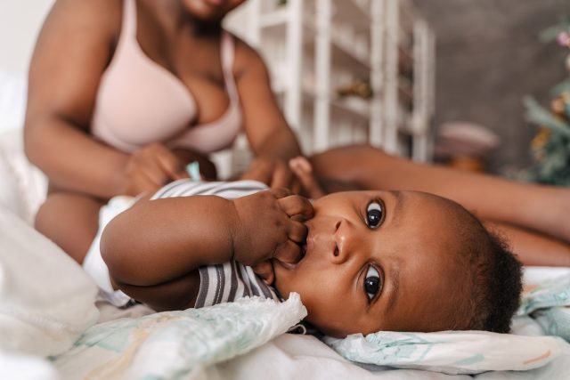 Portrait of cute black baby sucking fingers looking at camera