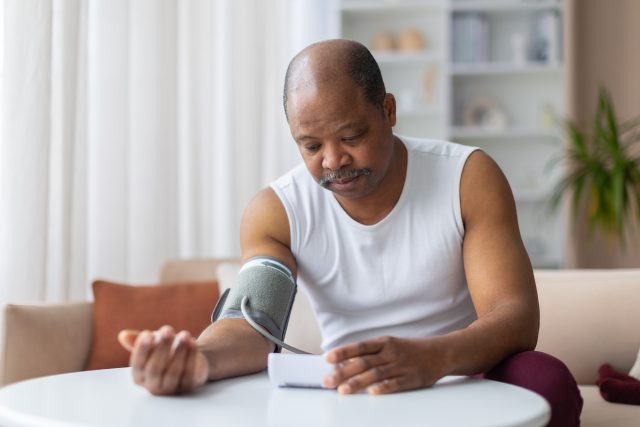 Mature African American man using blood pressure monitor on arm at home